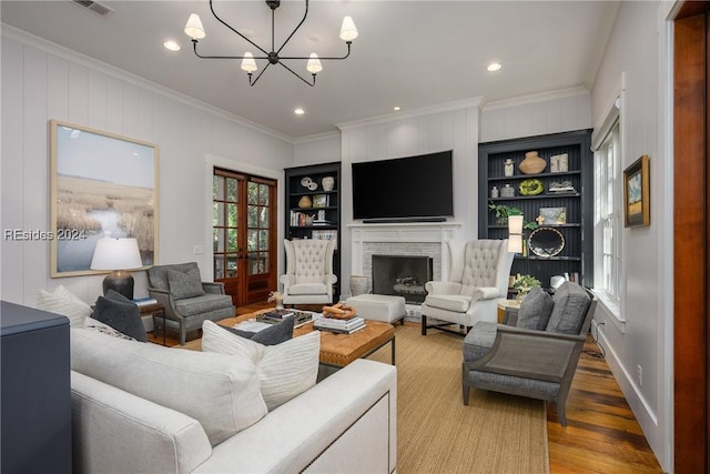 living room with a fireplace, hardwood / wood-style flooring, crown molding, an inviting chandelier, and built in shelves