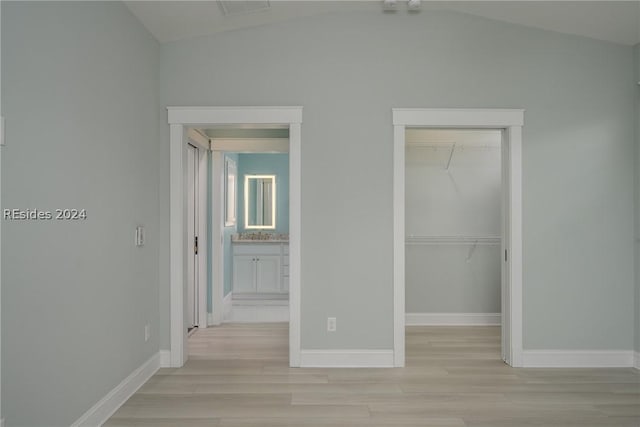 unfurnished bedroom with vaulted ceiling, a spacious closet, a closet, and light hardwood / wood-style flooring