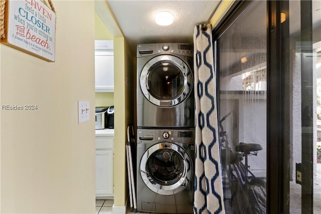 laundry room with light tile patterned floors, a textured ceiling, and stacked washing maching and dryer