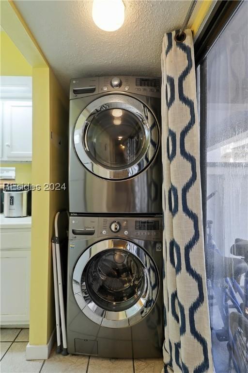 washroom featuring stacked washing maching and dryer, light tile patterned flooring, and a textured ceiling