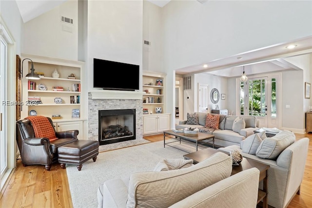 living room with a stone fireplace, high vaulted ceiling, light wood-type flooring, and built in shelves