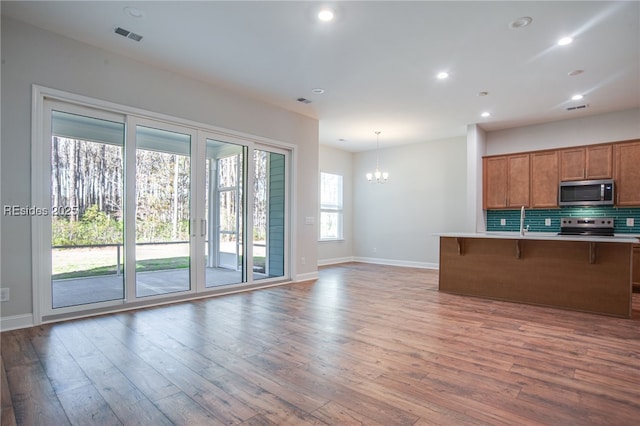 kitchen with hardwood / wood-style flooring, appliances with stainless steel finishes, backsplash, a kitchen breakfast bar, and decorative light fixtures