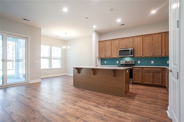 kitchen featuring dark hardwood / wood-style floors, a kitchen bar, hanging light fixtures, stainless steel appliances, and a center island with sink