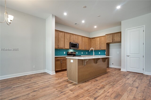 kitchen featuring stainless steel appliances, an island with sink, pendant lighting, and light hardwood / wood-style floors