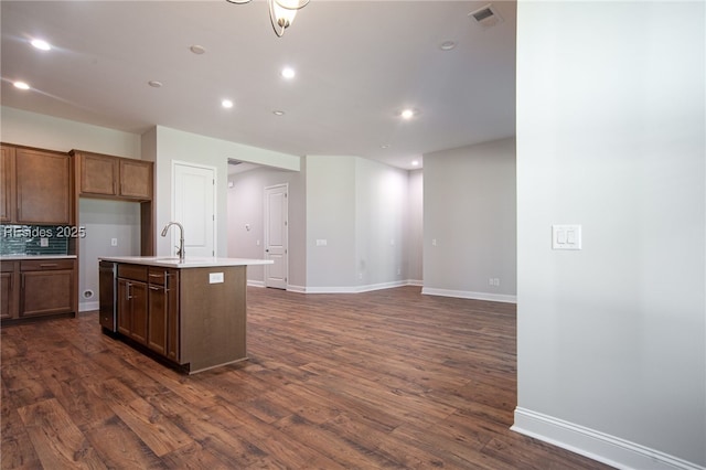 kitchen featuring a kitchen island with sink, sink, backsplash, and dark hardwood / wood-style flooring