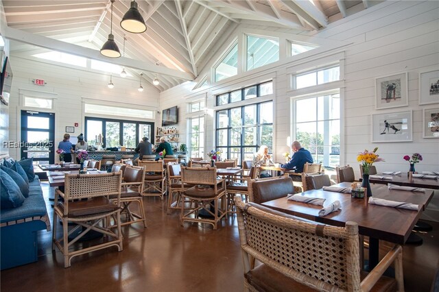 dining room with wooden walls, high vaulted ceiling, and concrete floors