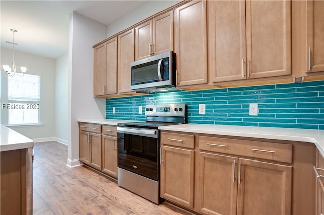 kitchen with appliances with stainless steel finishes, pendant lighting, a chandelier, decorative backsplash, and light hardwood / wood-style flooring