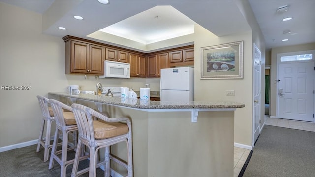 kitchen with light tile patterned floors, white appliances, a kitchen breakfast bar, light stone counters, and kitchen peninsula