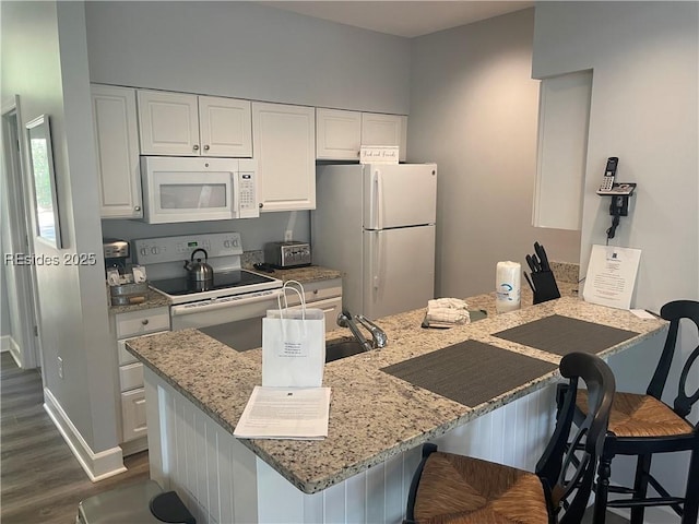 kitchen featuring a breakfast bar, light stone counters, white cabinets, and white appliances