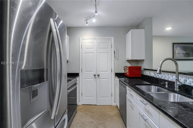 kitchen with sink, rail lighting, white cabinetry, stainless steel appliances, and dark stone counters