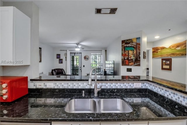 kitchen featuring white cabinetry, sink, kitchen peninsula, and dark stone counters