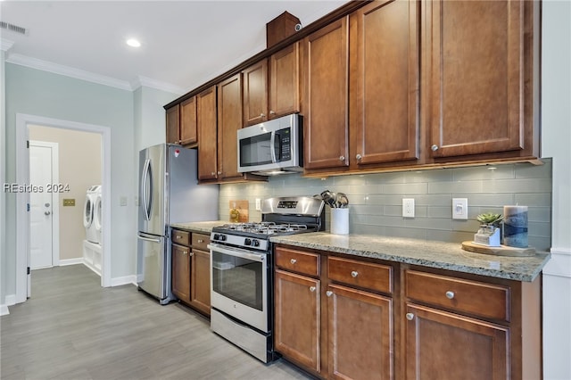 kitchen with separate washer and dryer, ornamental molding, stainless steel appliances, light stone countertops, and backsplash