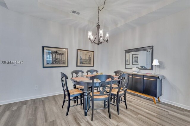 dining area with a notable chandelier, a tray ceiling, and light wood-type flooring