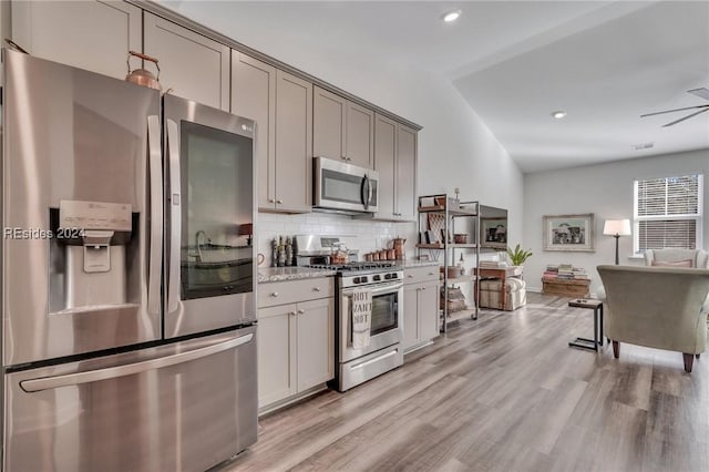 kitchen featuring gray cabinets, lofted ceiling, backsplash, stainless steel appliances, and light hardwood / wood-style flooring