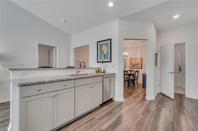 kitchen featuring sink, vaulted ceiling, light wood-type flooring, stainless steel dishwasher, and light stone countertops