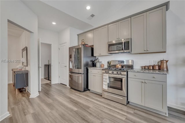 kitchen featuring tasteful backsplash, gray cabinetry, light hardwood / wood-style floors, stainless steel appliances, and light stone countertops