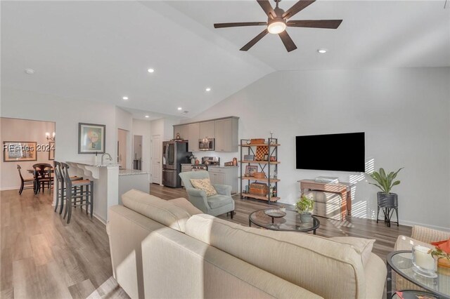 living room with lofted ceiling, ceiling fan with notable chandelier, and light hardwood / wood-style floors