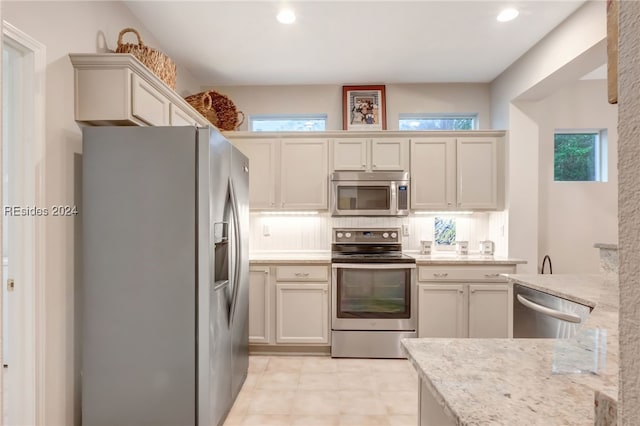 kitchen with light stone counters, appliances with stainless steel finishes, backsplash, and a wealth of natural light