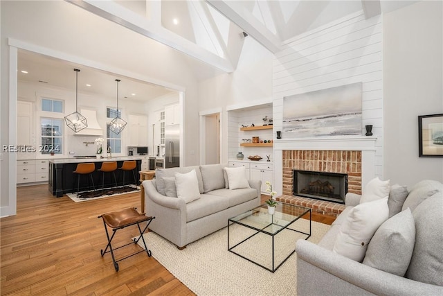 living room featuring sink, high vaulted ceiling, a brick fireplace, light wood-type flooring, and beamed ceiling