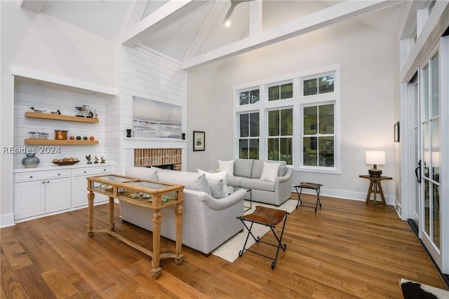 living room with high vaulted ceiling, beamed ceiling, a brick fireplace, a healthy amount of sunlight, and light wood-type flooring