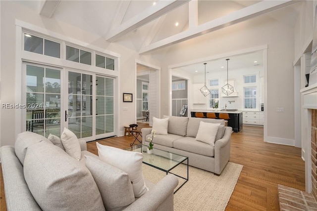 living room with beamed ceiling, wood-type flooring, high vaulted ceiling, and a brick fireplace