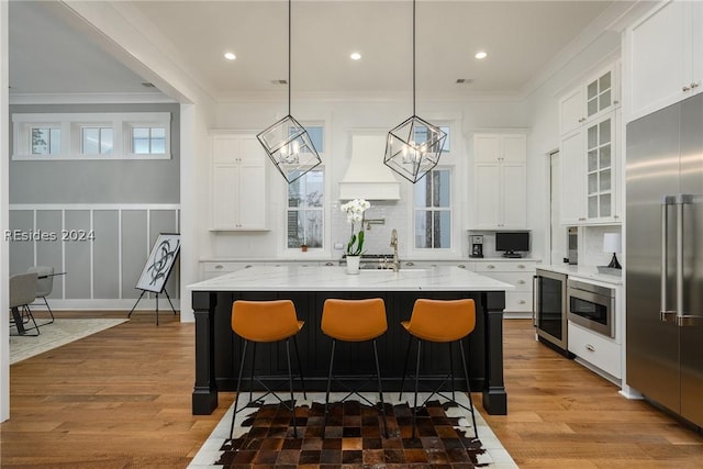 kitchen featuring decorative light fixtures, wine cooler, built in refrigerator, light stone countertops, and a center island with sink