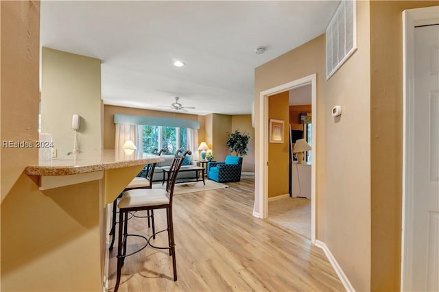 kitchen with ceiling fan, a kitchen bar, and light hardwood / wood-style flooring