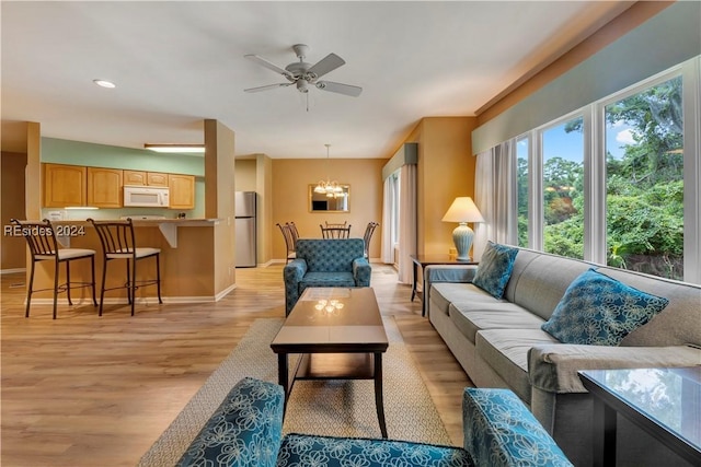 living room with ceiling fan with notable chandelier and light wood-type flooring