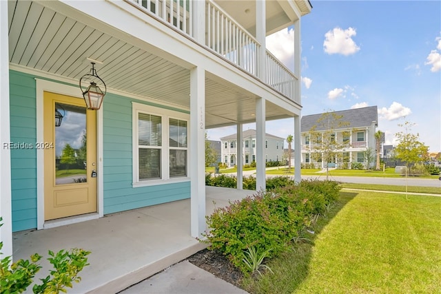 entrance to property featuring a lawn, a balcony, and a porch