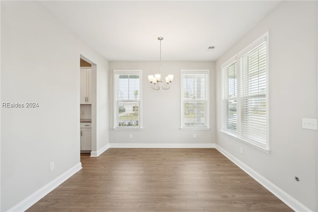 unfurnished dining area with a notable chandelier, dark wood-type flooring, and a wealth of natural light