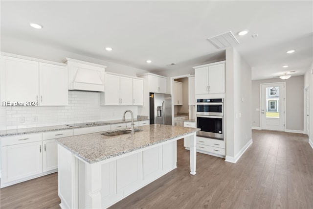 kitchen with sink, white cabinetry, light stone counters, a center island with sink, and appliances with stainless steel finishes