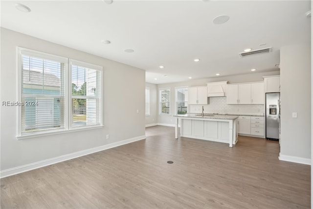 kitchen with white cabinetry, a kitchen island with sink, tasteful backsplash, stainless steel fridge with ice dispenser, and light wood-type flooring