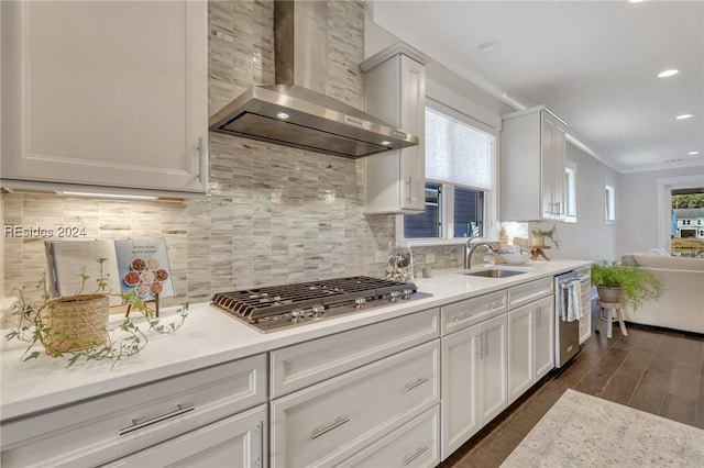 kitchen featuring wall chimney range hood, sink, white cabinetry, stainless steel appliances, and decorative backsplash