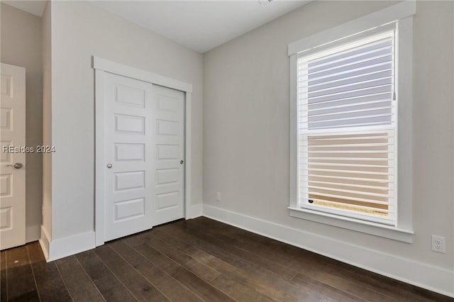 unfurnished bedroom with multiple windows, dark hardwood / wood-style floors, and a closet