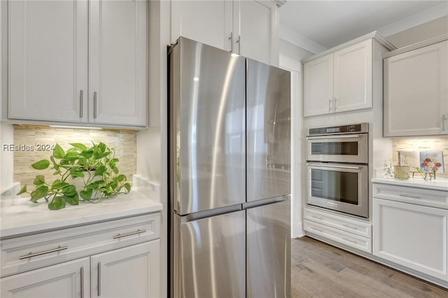 kitchen with backsplash, appliances with stainless steel finishes, light hardwood / wood-style flooring, and white cabinets