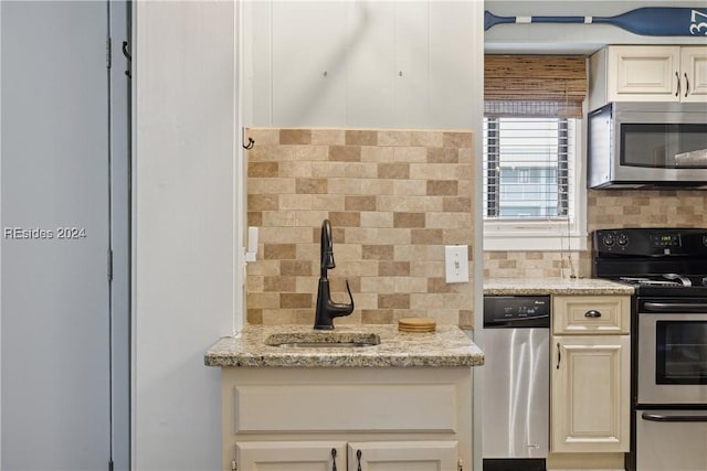 kitchen featuring sink, appliances with stainless steel finishes, backsplash, light stone counters, and cream cabinetry