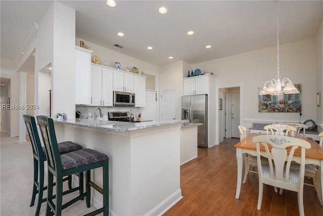 kitchen with white cabinetry, tasteful backsplash, kitchen peninsula, stainless steel appliances, and light stone countertops