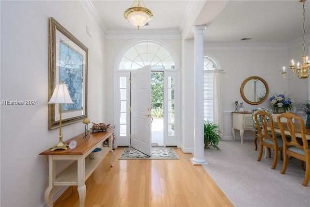 carpeted foyer entrance with decorative columns, crown molding, and a notable chandelier