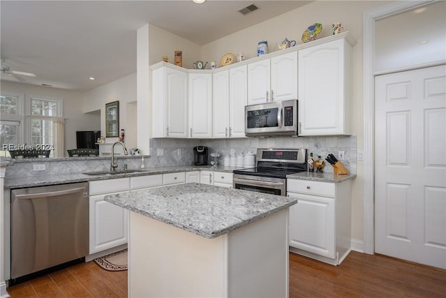 kitchen featuring sink, stainless steel appliances, light stone counters, white cabinets, and a kitchen island