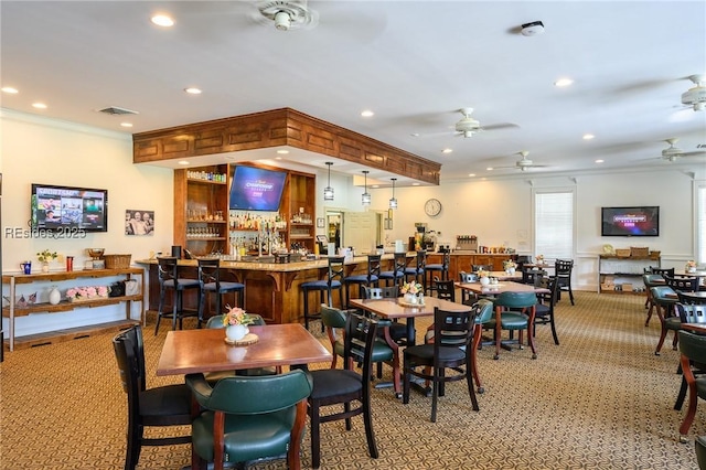 dining room with ceiling fan, ornamental molding, bar area, and light carpet