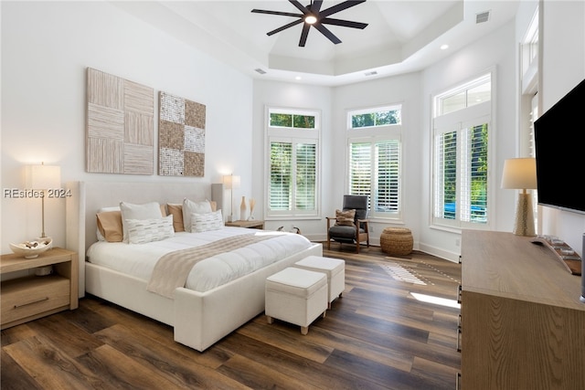 bedroom featuring dark wood-type flooring, ceiling fan, a tray ceiling, and a towering ceiling