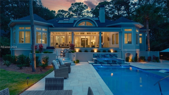 back house at dusk featuring a patio and solar panels