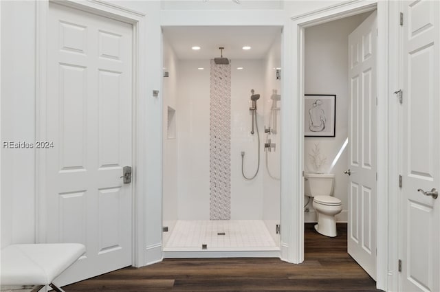 bathroom with hardwood / wood-style flooring, toilet, and tiled shower