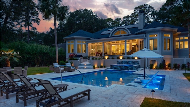 back house at dusk featuring a swimming pool with hot tub and a patio area