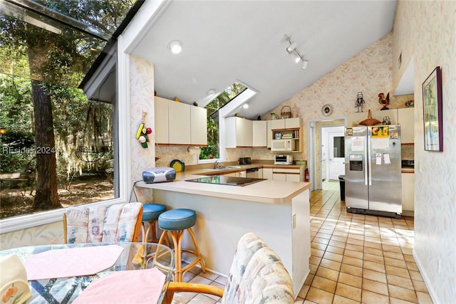 kitchen featuring a breakfast bar area, stainless steel fridge with ice dispenser, light tile patterned floors, kitchen peninsula, and vaulted ceiling with skylight