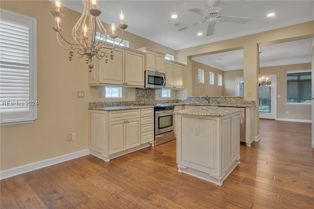 kitchen with decorative light fixtures, kitchen peninsula, stainless steel appliances, light stone countertops, and cream cabinets