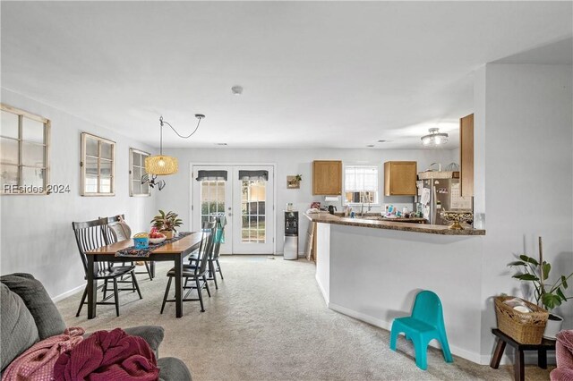 interior space with stainless steel refrigerator, hanging light fixtures, french doors, light colored carpet, and kitchen peninsula