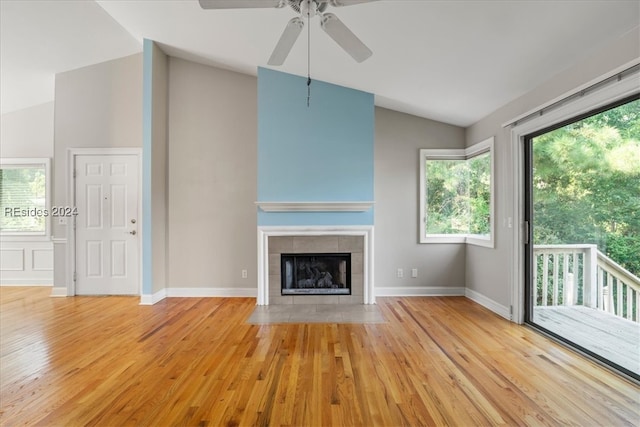 unfurnished living room with ceiling fan, a tile fireplace, vaulted ceiling, and light hardwood / wood-style flooring