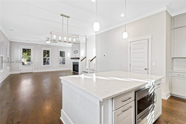 kitchen with tasteful backsplash, decorative light fixtures, a center island, stainless steel microwave, and ornamental molding