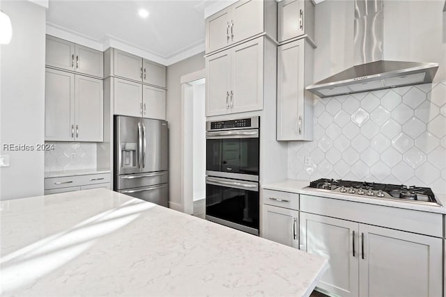 kitchen featuring wall chimney range hood, decorative backsplash, light stone countertops, and appliances with stainless steel finishes